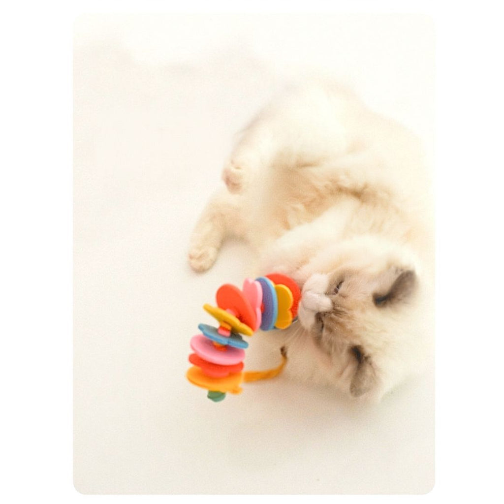 Fluffy white cat rolling on its back playing with the R.U.S.H. rainbow felt silvervine toy