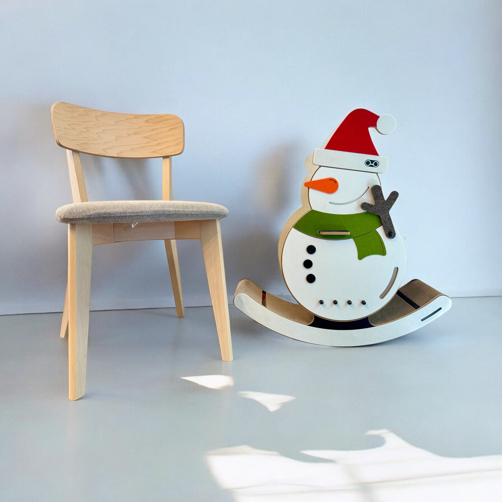 Lifestyle shot showing the scale of the large 6.6 kg snowman cat rocker placed next to a standard wooden dining room chair.
